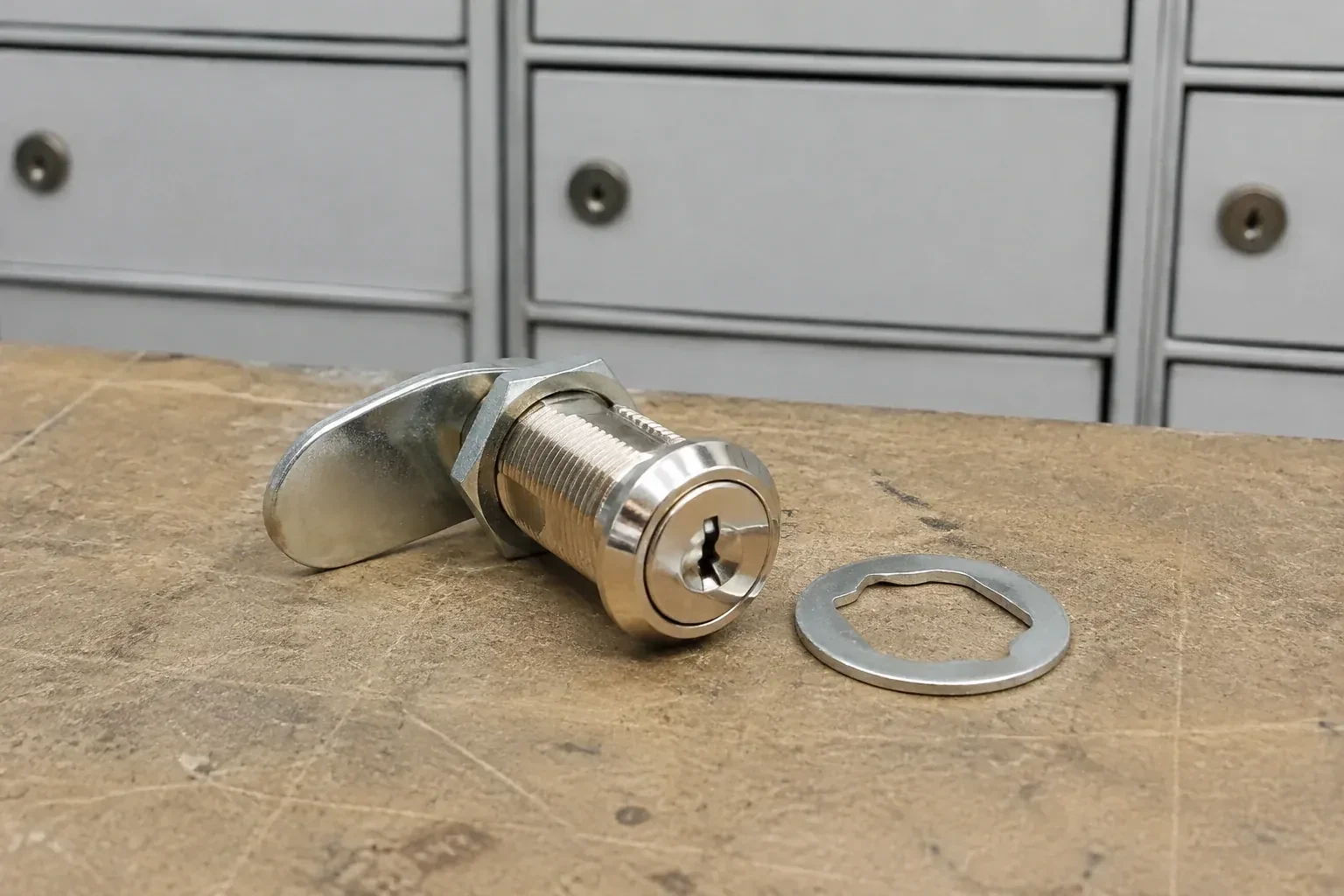 Detached threaded cam lock and mounting washer on a workbench in front of closed mail compartments. — Mailbox Lock Replacement, Peterborough